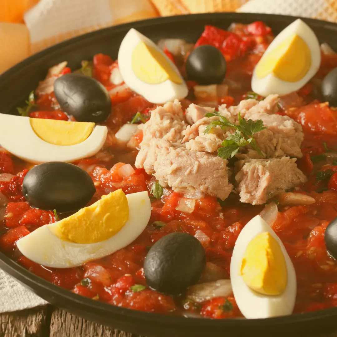 Salade Mechouia mit Tomaten, Thunfisch, schwarzen Oliven und geviertelten Eiern auf schwarzem Teller