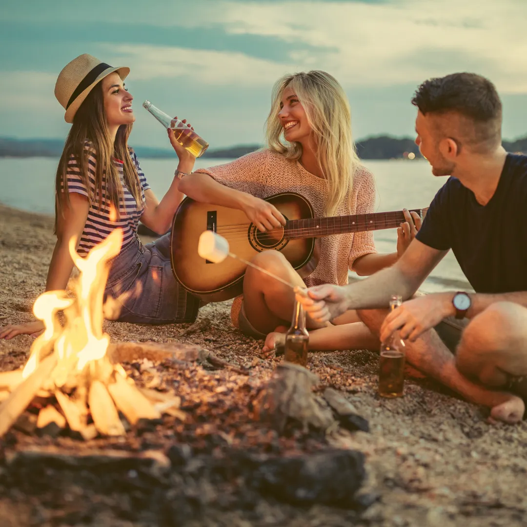 Drei Personen am Lagerfeuer an einem Strand – entspannte Atmosphäre mit Sonne und Olivenöl