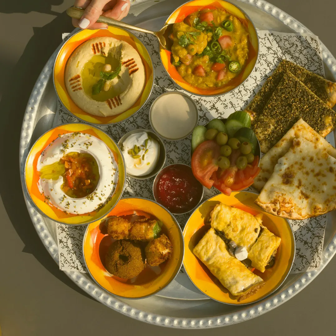 Breakfast plate with hummus, vegetables, flatbread, dips and small oriental dishes on a metal tray