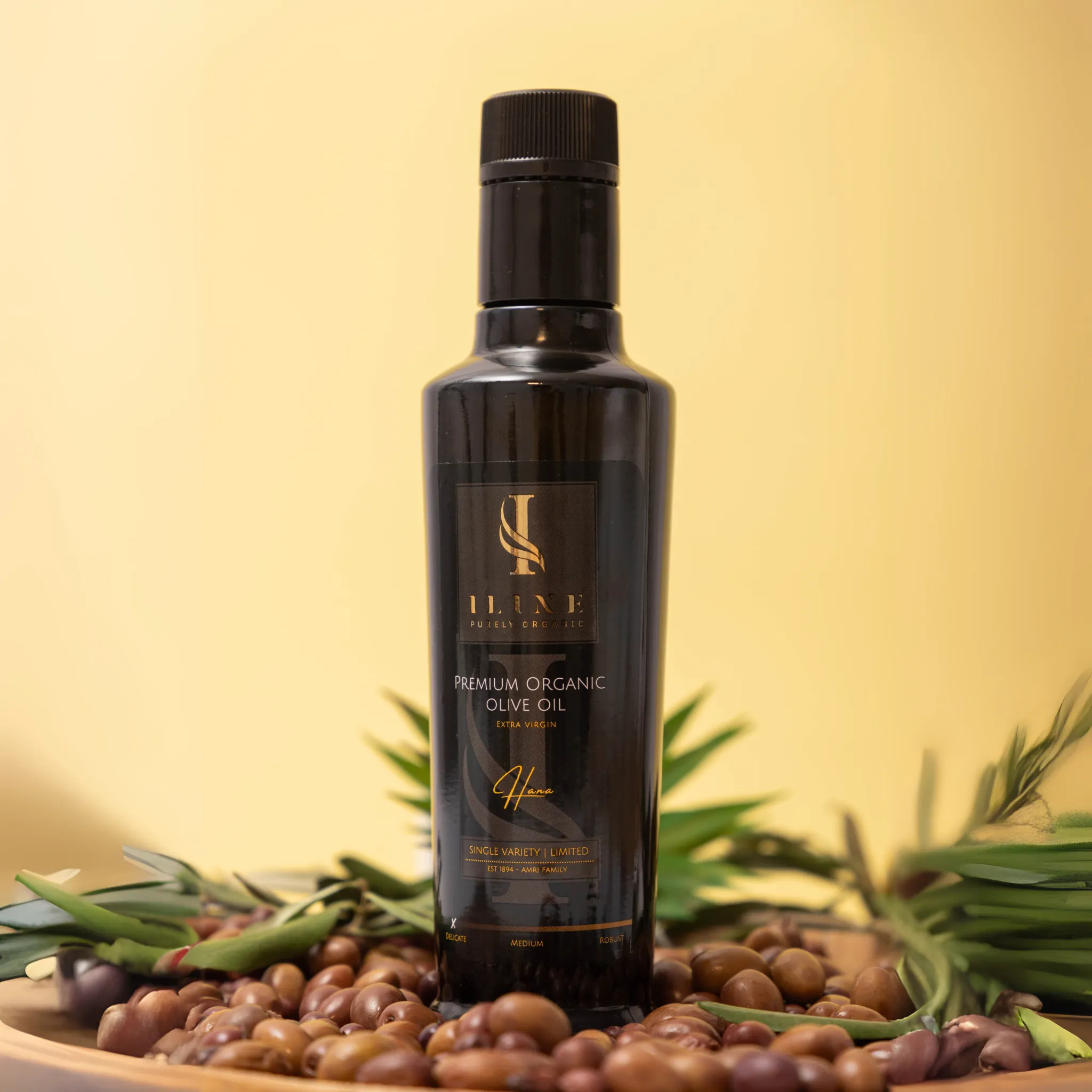 250 ml bottle of Hana Delicate organic olive oil from Iline Organic on a wooden board with olives and twigs
