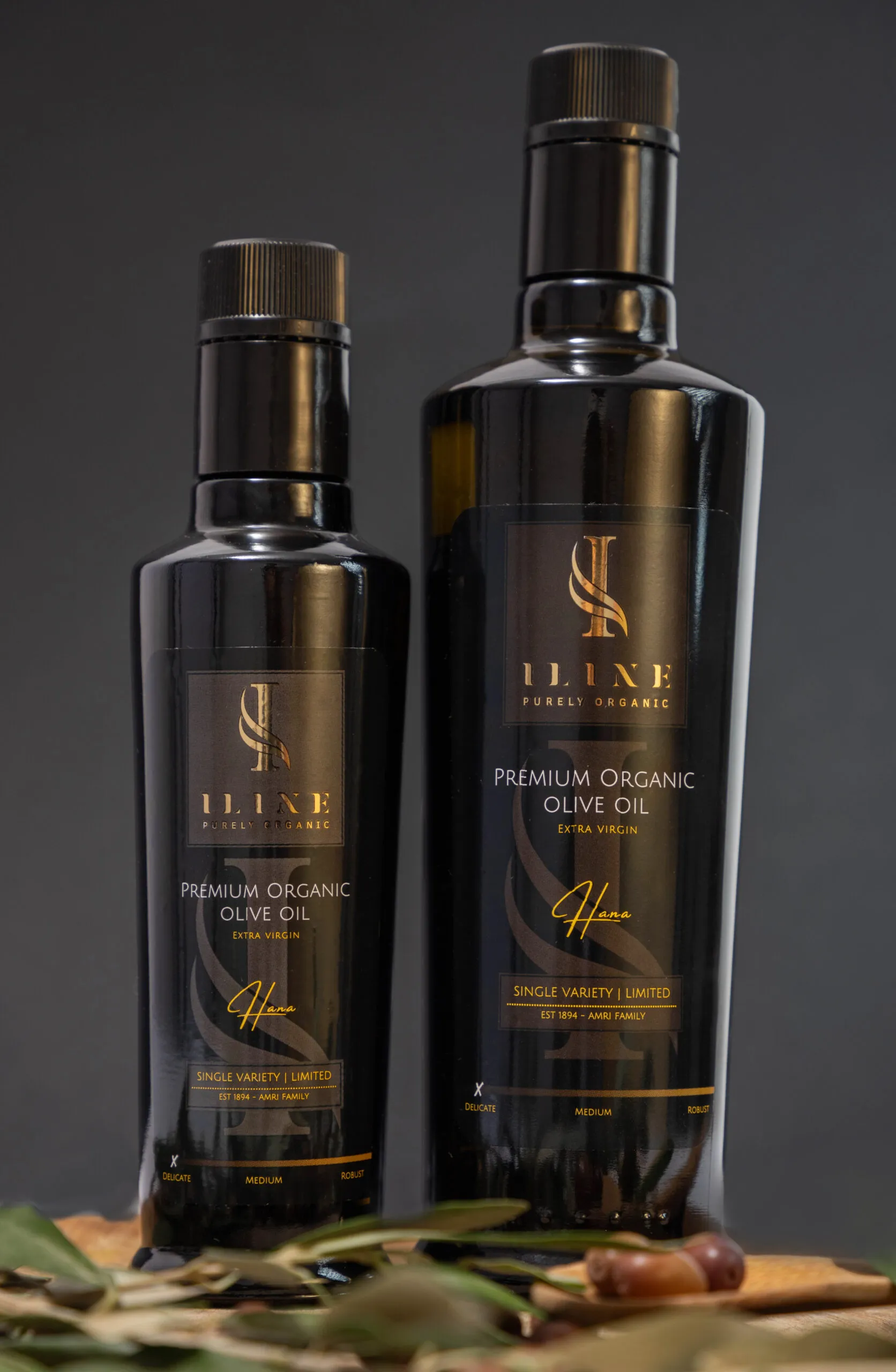 Zwei Flaschen Iline Organic Hana Delicate Bio-Olivenöl mit 250 ml und 500 ml vor dunklem Hintergrund.