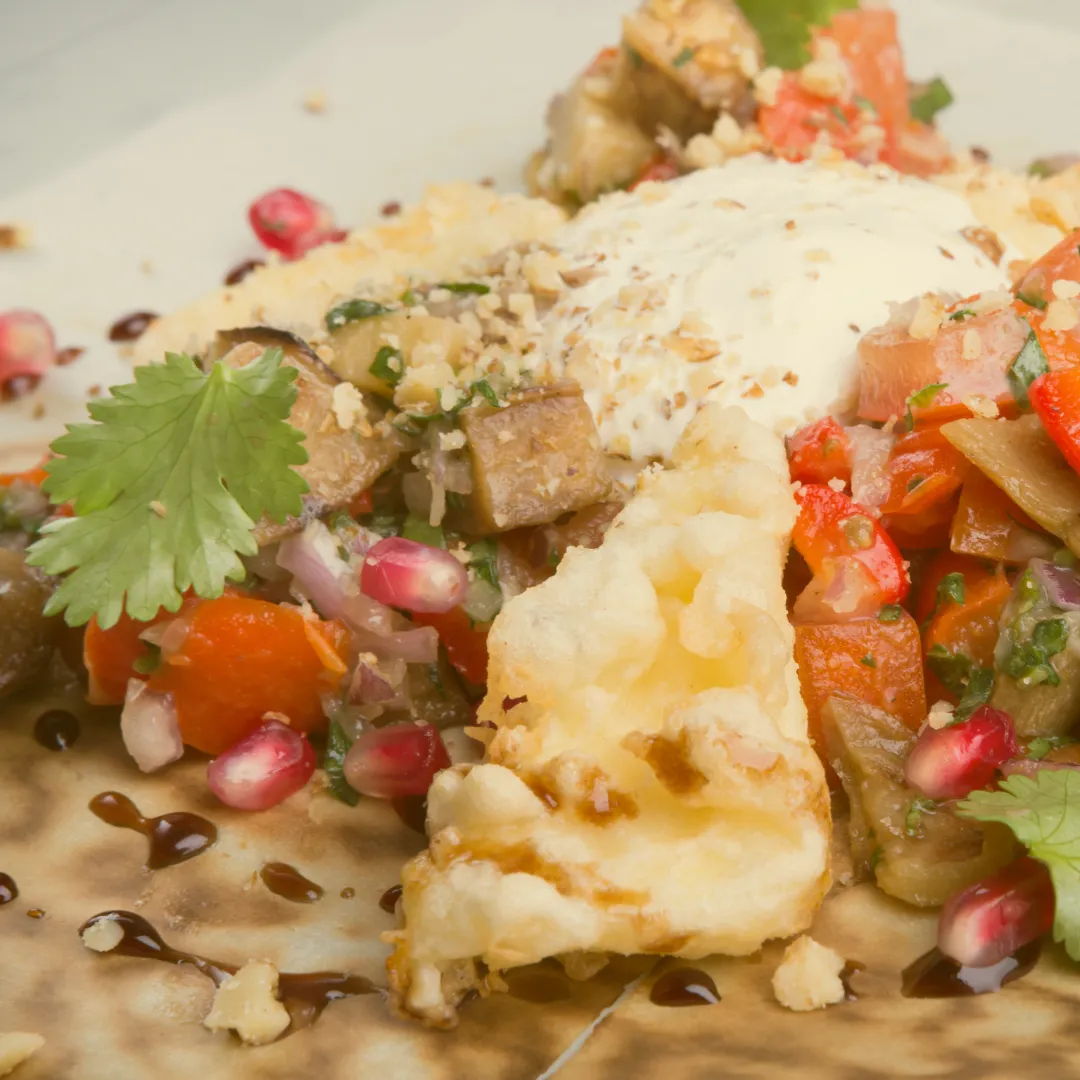 Piatto vegano con verdure grigliate, semi di melograno, erbe aromatiche e una copertura cremosa