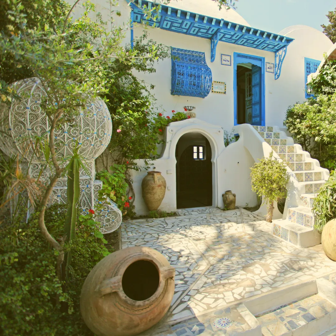 Weiß getünchte Häuser mit blühender Bougainvillea und Palme vor blauem Meer und klarem Himmel, symbolisiert mediterranes Lebensgefühl und steht für Olivenöl in Bag-in-Box
