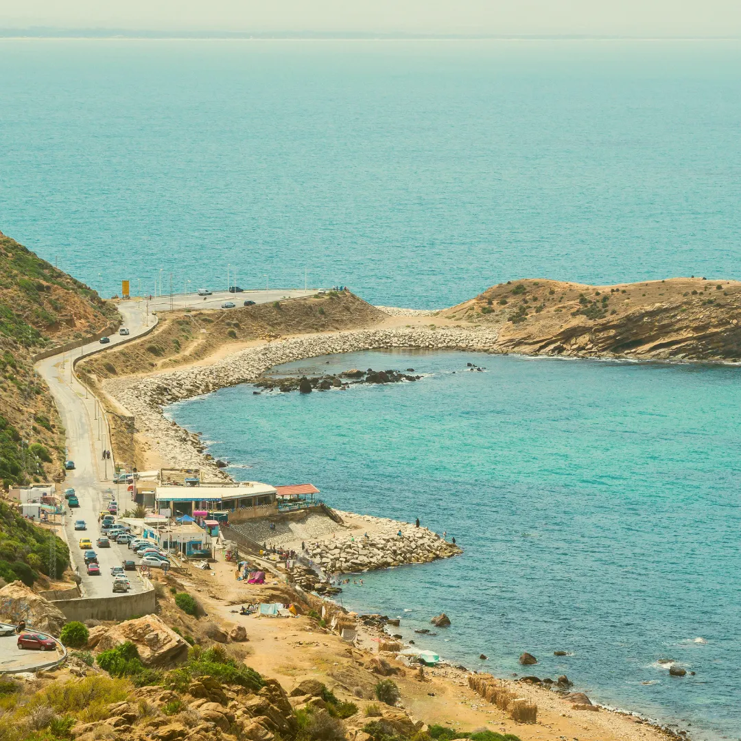 Blick auf eine mediterrane Küstenstraße mit türkisblauem Meer und kleinen Häusern – Ort, an dem viele Iline Organic Ideen entstanden sind	